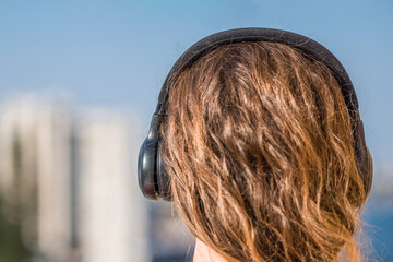 woman in a pink shirt standing on the balcony and listening music in a headphones against the city background
