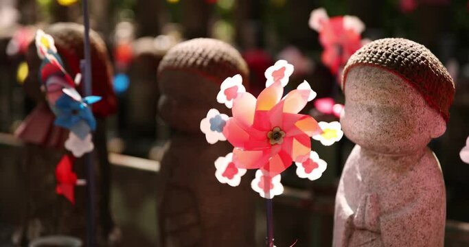 A slow motion of moving colorful windmills with Jizo statue daytime closeup
