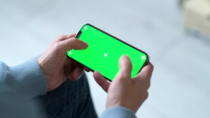  man playing game using Phone smartphone viewing green screen on phone horizontal press chroma key online close up in two hands at home 