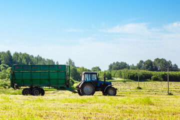 Tractor with a trailer in the field for agricultural work. Hay making, grassland. Copy space.