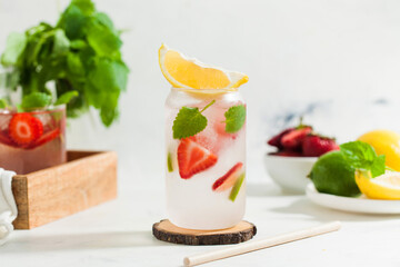 A refreshing summer drink with strawberries, lemon and mint in a glass on a light background. Strawberry lemonade