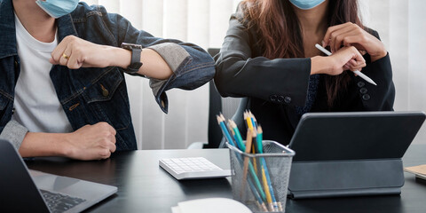 Two young diverse business colleagues wearing face protective masks bumping elbows, greeting each other while working during covid 19 quarantine.