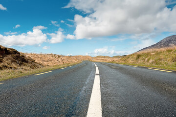 Small narrow asphalt road in Connemara, county Galway, Ireland. With beautiful nature view. Irish landscape. Cloudy sky. Low angle of view