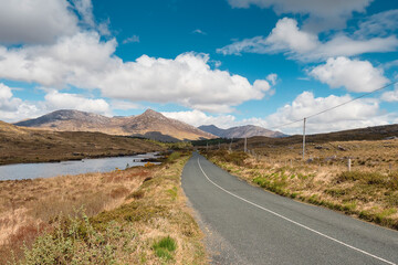 Small narrow asphalt road in Connemara, county Galway, Ireland. With beautiful nature view. Irish landscape. Cloudy sky. Warm sunny day. Travel concept
