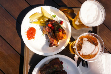 Pork ribs on a tray and light beer on wooden table background. Street food. Festival food on a sunny day