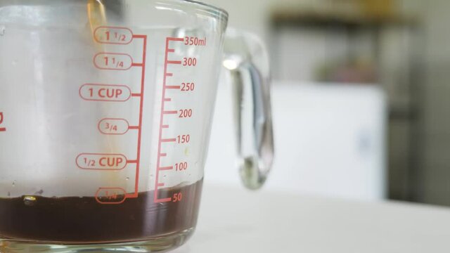 Pouring hot espresso coffee water into a glass measuring cup until it reaches 200ml.