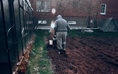 A farmer plows the land with a cultivator. Agriculture in the garden and garden. Vegetable and fruit plantation