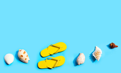 Yellow flip flops with exotic sea shells on blue background. Summer background concept