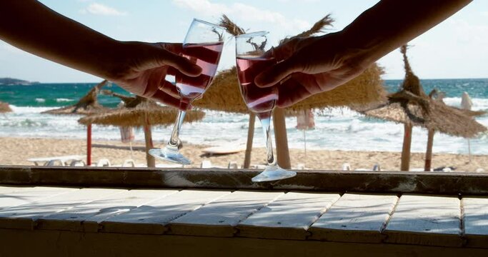 Hands hold glasses with rose wine to cheering on the beach bar on a hot summer day, 4k slow motion