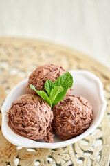 Chocolate ice cream with mint leafe. three balls in a white bowl on a vintage table.