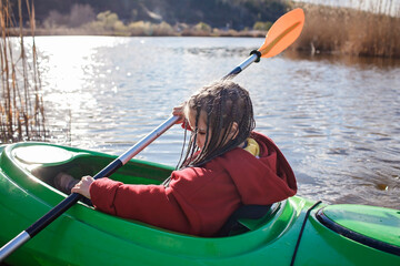 Happy preteen girl kayaking alone on the river, paddle in the hand, summer camp activity, extreme sport, outdoor lifestyle