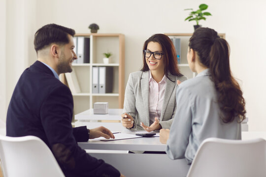 Woman Financial Advisor Giving Consultation To Family Couple About Buying House. Smiling Investment Broker Or Bank Worker Consulting Customers Making Loan Offer Or Selling Insurance Sitting At Table