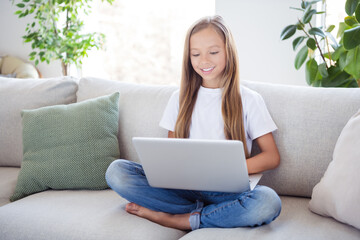 Photo of happy good mood cheerful little girl sit sofa browsing in laptop having great weekend at home house