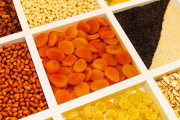 Dried fruits and nuts in a wooden tray. Dried apricots and peanuts on the counter in the store. Confectionery ingredients are available wholesale and retail. Close-up