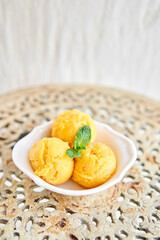 Mango ice cream with mint leaf. three balls in a white bowl on a vintage table. sorbet