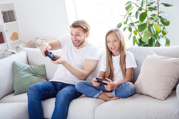 Photo of charming addicted daughter father wear casual sitting sofa holding playstation controllers indoors apartment house