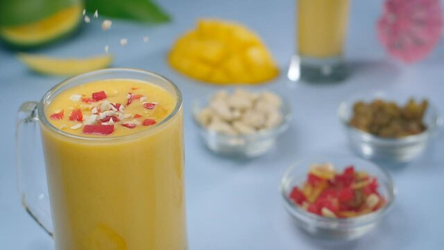 Crushed cashew nuts decorating delicious mango smoothie - summer drink India. Closeup shot of a clear glass mug with healthy Aam Lassi  dry fruits  and tutti frutti placed together