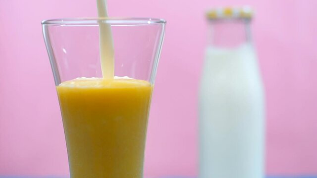 Creamy milk is poured into a clear glass of mango shake - a healthy drink  Summer drink India. Closeup shot of a bottle of fresh milk kept near a glass of refreshing tropical Aam juice - summer fruit