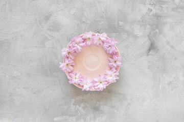 Empty small plate and fresh spring sakura flowers, minimalistic pastel pink and gray background. Tea party, drinking coffee or dessert recipe concept. Top view, flat lay, copy space