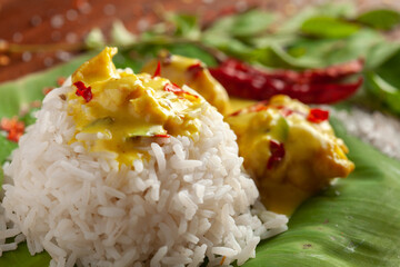 Close-up of Indian cooked rice with kadi or kadhi over the banana fresh green leaf. Garnished with curry-patta leaves and red chilli paper and salt.