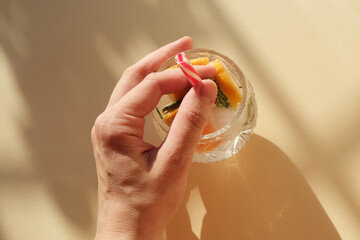 Hard seltzer alcoholic summer cocktail in a glass. Female hand holding glass of refreshing drink with grapefruit, rosemary and ice. Top view.