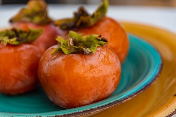 Close up view of a plate with persimmons, teal and orange color 