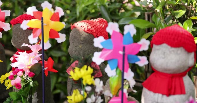 A slow motion of moving colorful windmills with Jizo statue daytime closeup