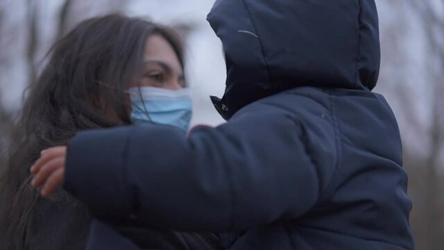 Mother holding baby toddler in arms while wearing covid-19 face mask outside during winter season