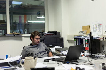 Erschöpfter Mitarbeiter sitz abends vor seinem Laptop im Büro und macht Überstunden