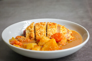 Japanese curry with rice, carrot, potato and deep fries chicken in white dish on table.