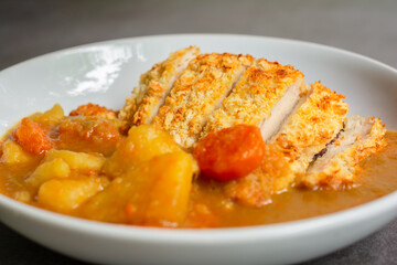 Japanese curry with rice, carrot, potato and deep fries chicken in white dish on table.