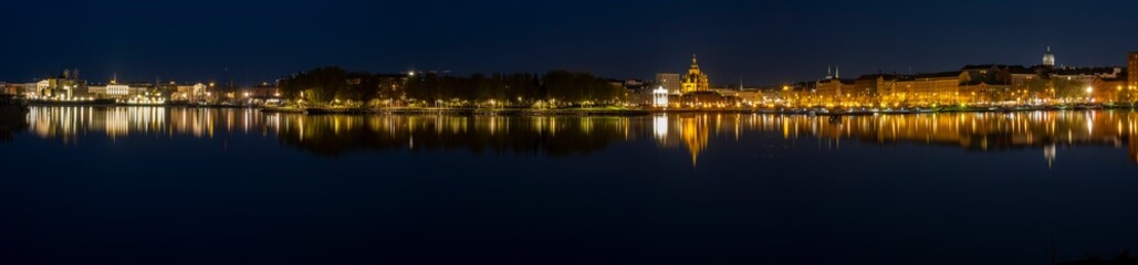 A beautiful panorama of downtown Helsinki waterfront with illuminated buildings casting reflections on the calm sea.