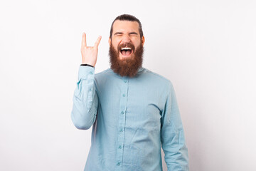 Excited bearded hipster man in blue shirt screaming and showing rock gesture