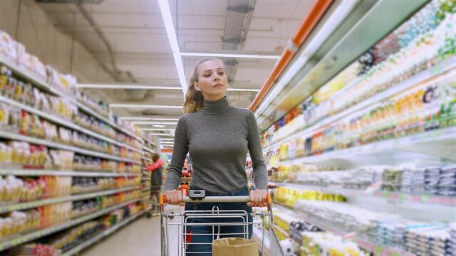 Young female walks between the shelves in a grocery store, visiting a supermarket, a woman walks with a shopping cart, 4k slow motion.