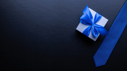 Fathers gift. White box with bow ribbon, blue bowtie or tie on dark background. Concept of Fathers Day greeting card, copy space for text.
