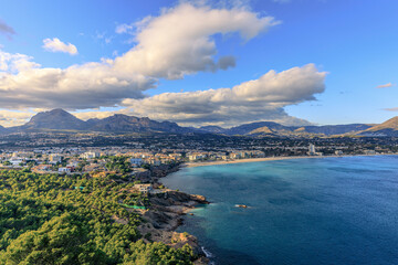 Obraz premium Wide view of the sea, beach, small town and mountains with blue sky and clouds.