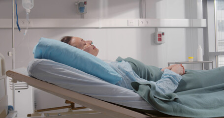 Side view of sick young woman with nasal cannula lying in hospital bed.