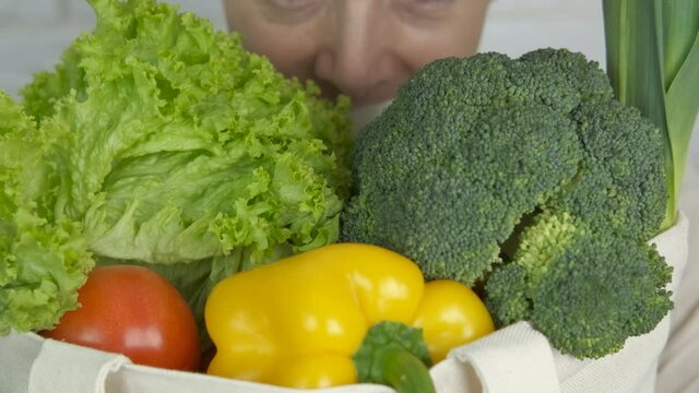 Eco farmer with a bag. A smiling vegan farmer hold a cotton shopper with organic vegetables in the room.