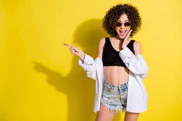 Photo of young happy smiling excited positive girl with curls pointing finger copyspace isolated on yellow color background