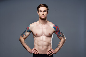 Fototapeta na wymiar handsome man with a naked pumped-up torso tattoos on his arms holds his hands on his belt