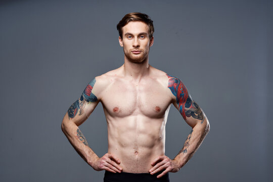 handsome man with a naked pumped-up torso tattoos on his arms holds his hands on his belt
