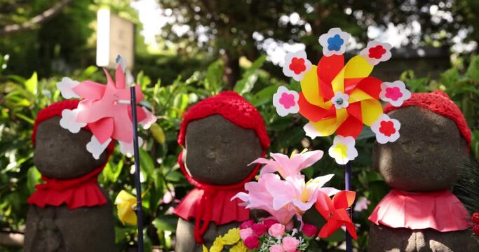 A slow motion of moving colorful windmills with Jizo statue daytime closeup