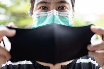 Asian lady girl is wearing a second mask,female putting double or a medical protective mask under a cloth mask for COVID-19 protection,safety from the risk of Coronavirus infection,health care concept