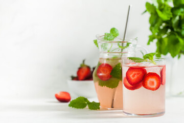 Homemade refreshing strawberry lemonade in glass and jug with fresh strawberries and mint leaves. Summer drink 