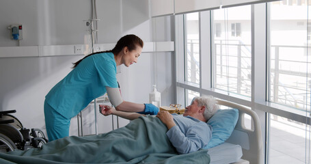 Female nurse setting up iv drip while treating senior man in hospital bed