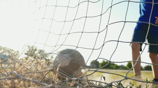 The young player rolls the ball into the net. Training day. Shots on goal. Street sports in a poor area of a city or village. The boy kicks the ball. Football concept.