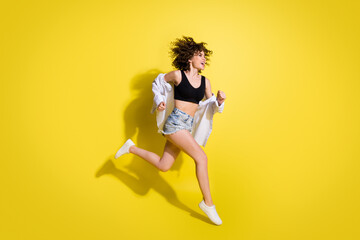Fototapeta na wymiar Full size profile photo of optimistic girl run wear top shorts shirt sneakers isolated on yellow background