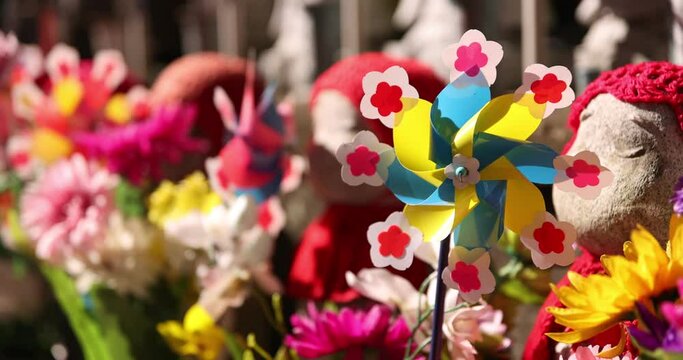 A slow motion of moving colorful windmills with Jizo statue daytime closeup