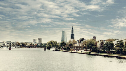 Obraz premium View of the river Main with skyscraper buildings and the Church Dreikönigskirche under construction in the distance. Frankfurt - Main in Germany with clouds sky. 