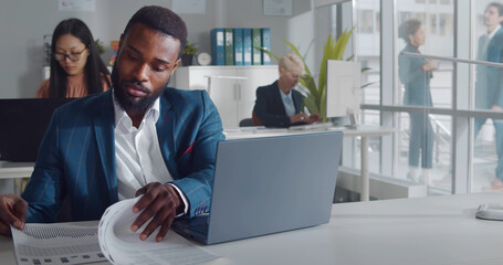 Handsome african entrepreneur using laptop sitting at desk in open space office